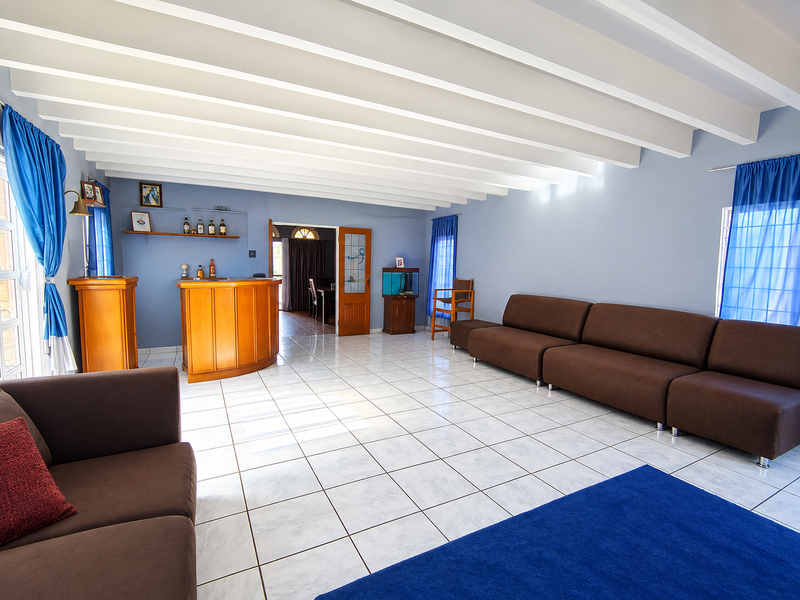 Spacious living room featuring exposed beam ceilings, ceramic tile flooring, and a built-in bar area, offering a versatile layout for entertaining.