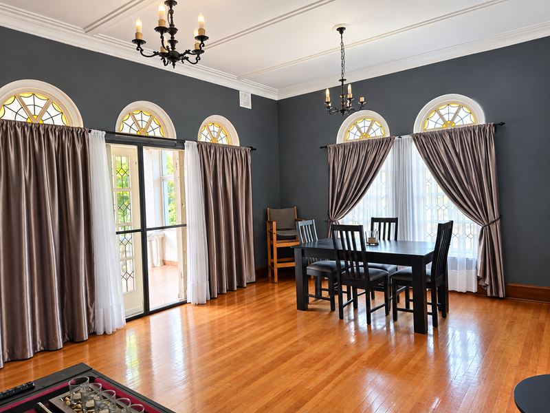 Elegant dining room featuring polished hardwood floors, dark charcoal walls, classic crown molding, and multiple arched windows with leaded glass accents.