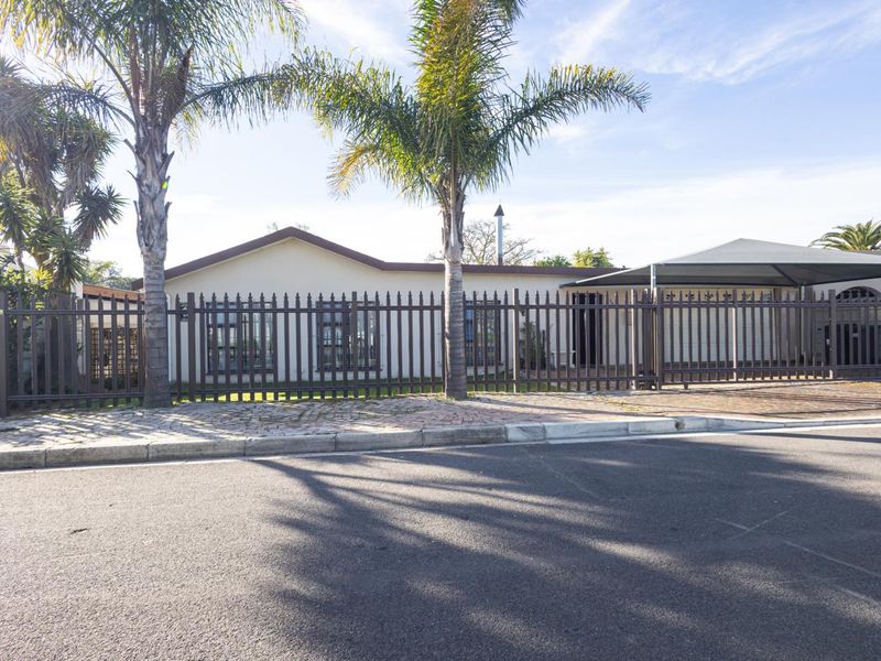 Front elevation of a residential house featuring a paved driveway, carport, and secure metal perimeter fencing.