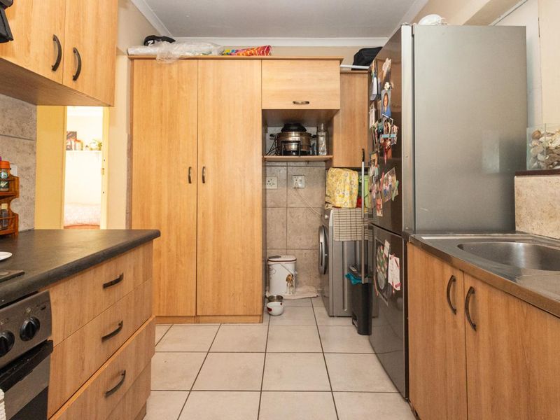A functional scullery area featuring laminate cabinetry, tiled flooring, a stainless steel sink, and built-in oven, providing additional prep and storage space.