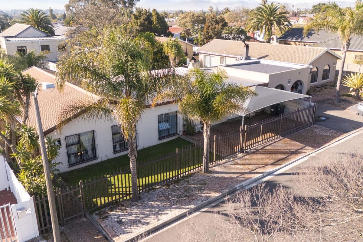 Aerial view of the property featuring a tiled roof, paved driveway, carport, and secure perimeter fencing with window security bars.