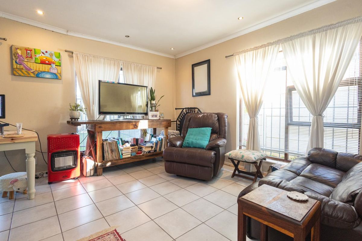 A bright living room featuring tiled flooring, recessed downlighting, and large windows with curtain treatments, offering a functional and well-lit living space.