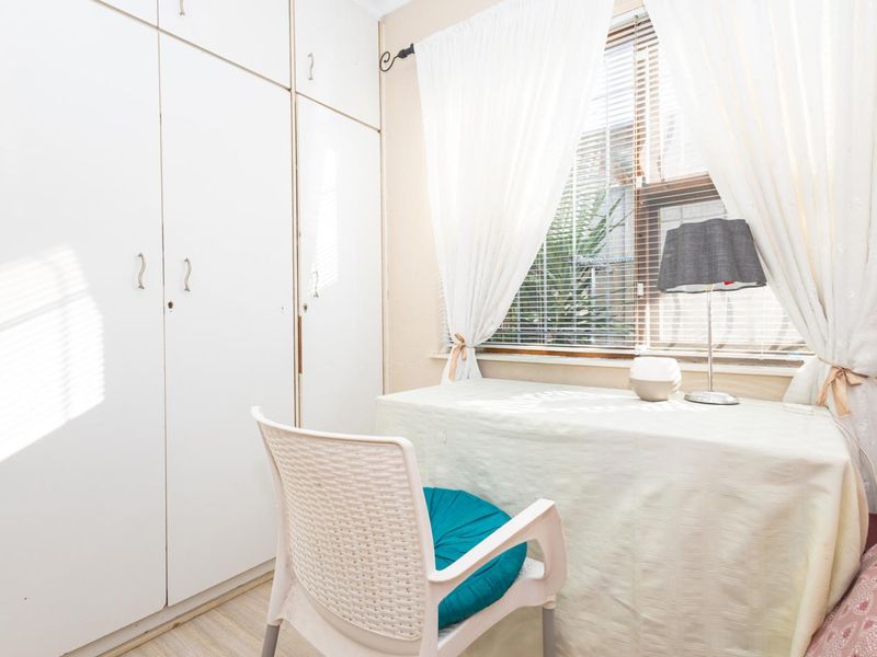 A bedroom featuring built-in cupboards and a window with venetian blinds, providing natural light and storage space.