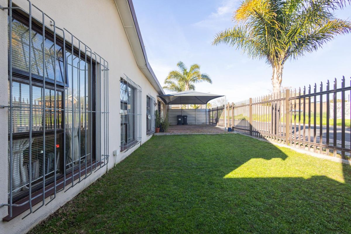 A well-maintained rear garden featuring a lawn, paved area with a shade sail, and secure metal perimeter fencing.
