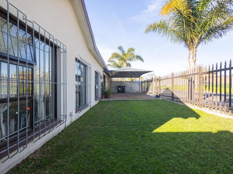 A well-maintained rear garden featuring a lawn, paved area with a shade sail, and secure metal perimeter fencing.