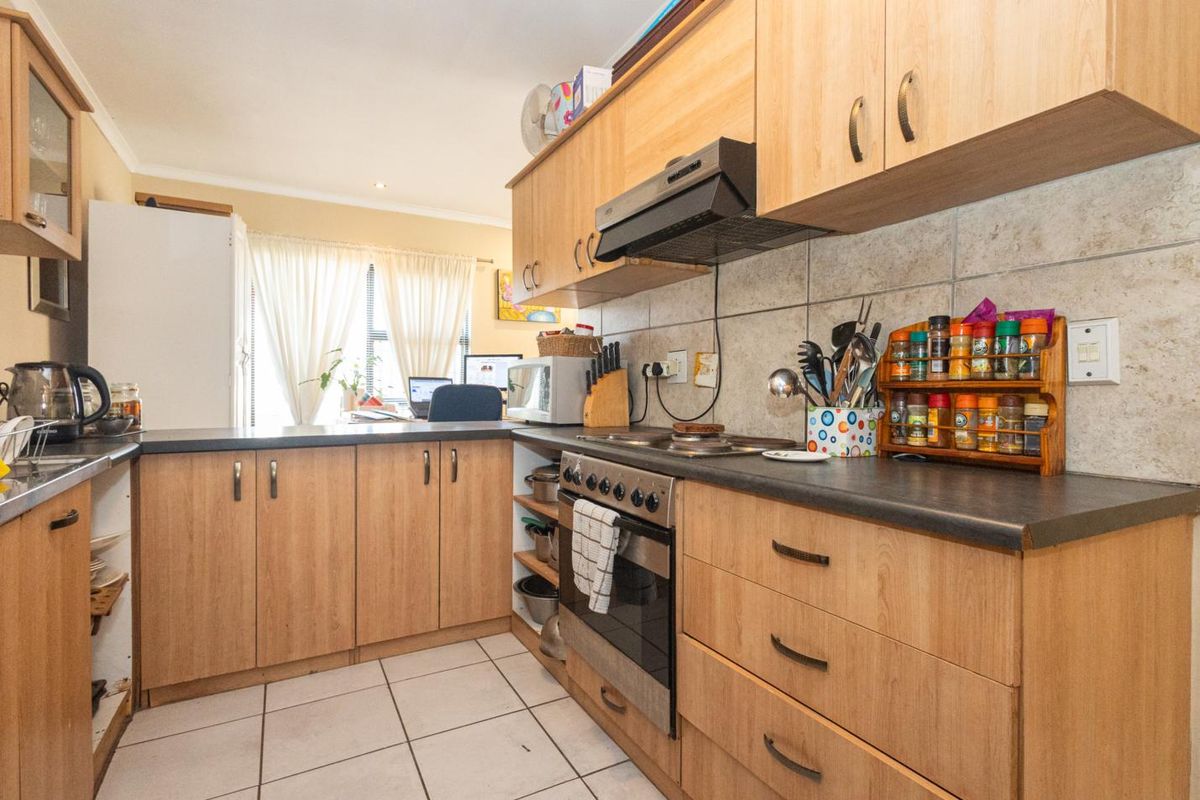 A functional kitchen featuring light wood-finish cabinetry, built-in oven with extractor fan, stone-look wall tiles, and durable tiled flooring.