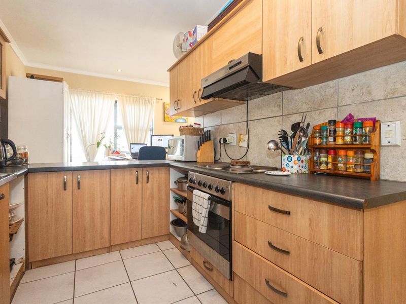 A functional kitchen featuring light wood-finish cabinetry, built-in oven with extractor fan, stone-look wall tiles, and durable tiled flooring.