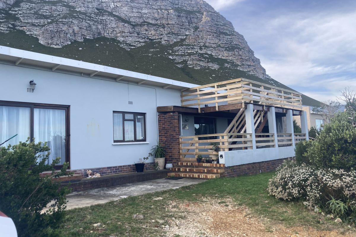 Rear exterior view of the property featuring a timber deck, staircase, and concrete patio set against a mountain backdrop.