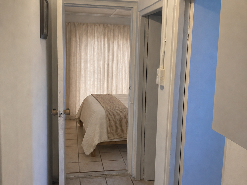 A narrow hallway with tiled flooring and exposed electrical conduit, providing access to adjacent rooms including a bedroom.