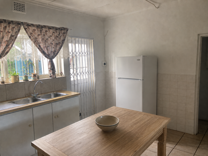 A functional kitchen featuring a double bowl sink, tiled splashbacks, and ceramic flooring, offering a practical layout with potential for modern cosmetic updates.