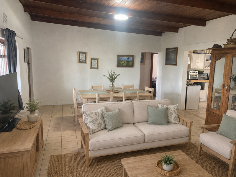 Open plan living and dining area featuring exposed timber beam ceilings and ceramic floor tiles, with an adjacent kitchen visible.