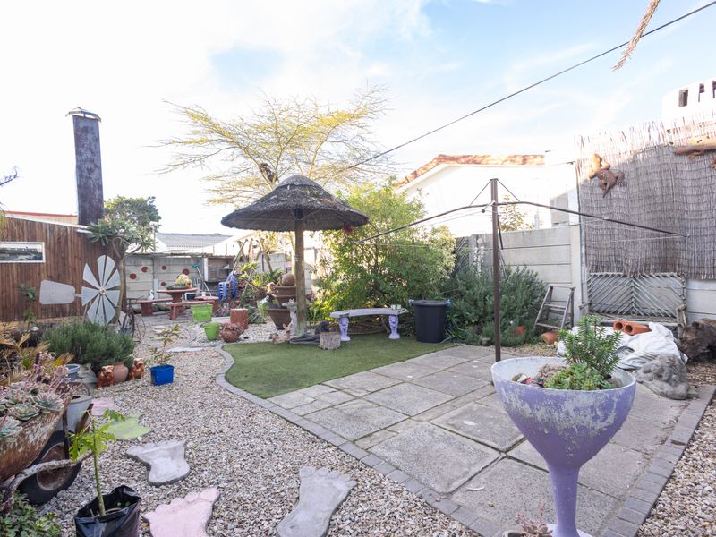 A rear garden area featuring a mix of gravel and paved sections, a rotary clothesline, and a thatched umbrella structure.