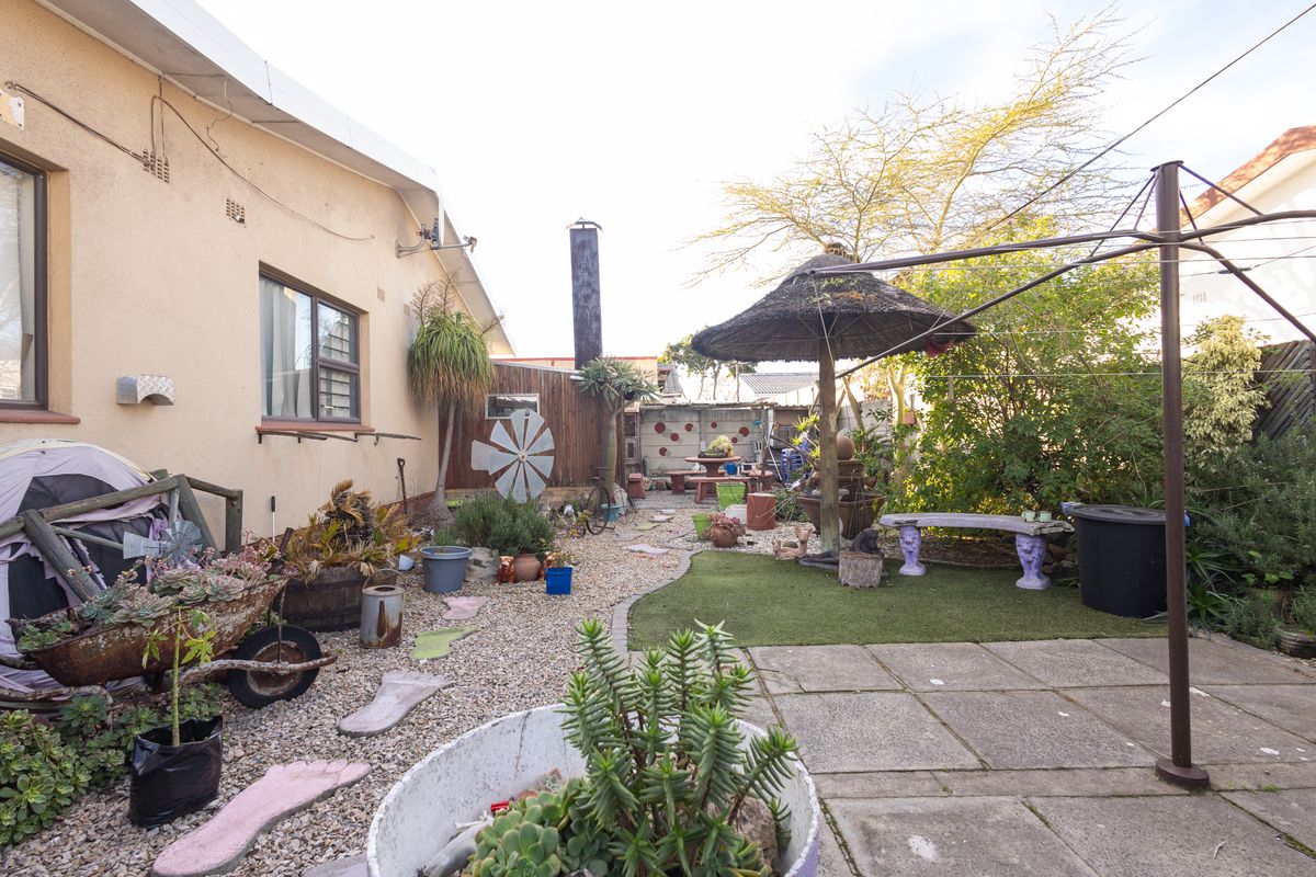 Rear garden area featuring a paved patio, artificial lawn section, gravel landscaping, and an external chimney stack against the house wall.