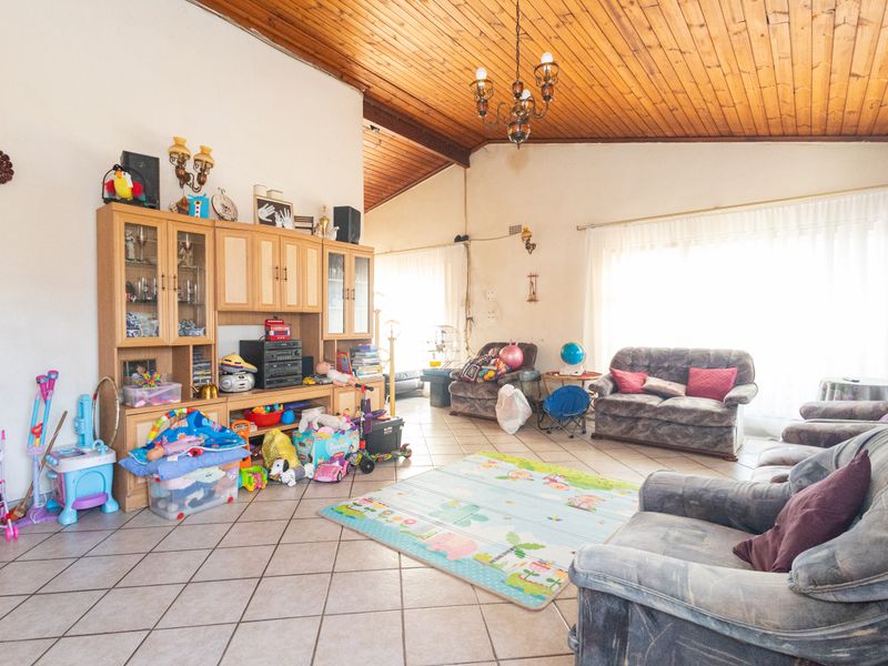 Spacious living room featuring a vaulted timber ceiling, ceramic floor tiles, and built-in cabinetry, offering a versatile layout with abundant natural light.