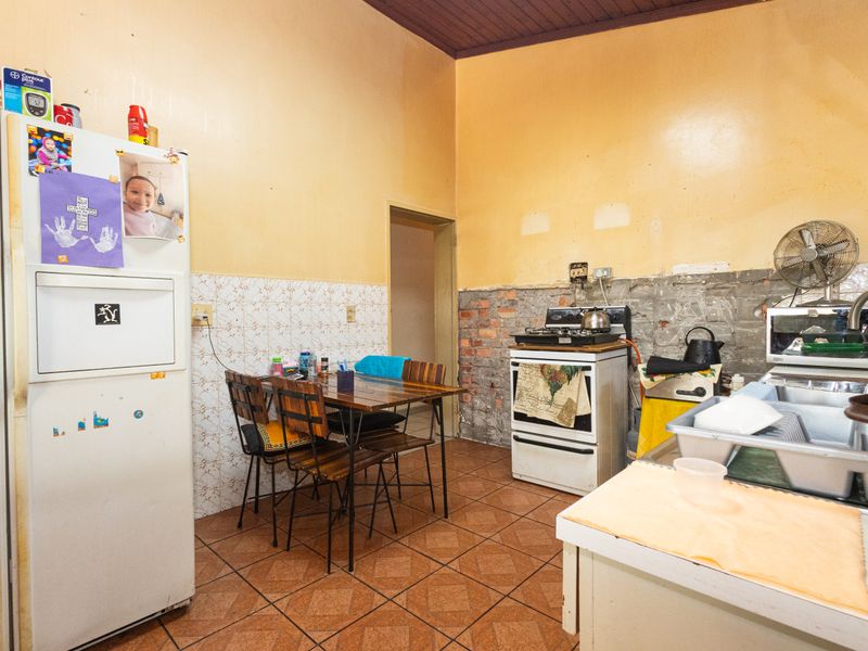 A functional kitchen space featuring tiled flooring, a freestanding stove, and a stainless steel sink, currently requiring wall finishing and cosmetic updates.