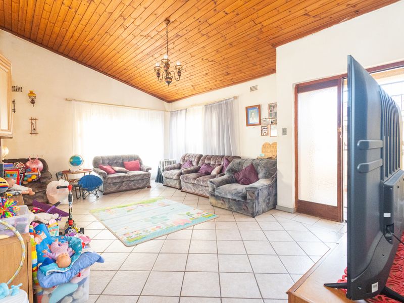 Spacious living room featuring a high timber-clad vaulted ceiling, ceramic tiled flooring, and direct access to the exterior through a glass-panelled door.