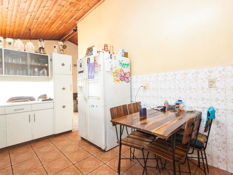 A functional kitchen featuring timber ceilings, tiled flooring, and a tiled splashback, offering potential for a modern renovation to update the dated finishes.