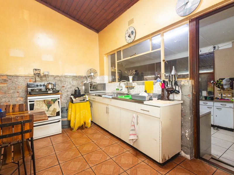 A dated kitchen featuring exposed brick walls, timber ceiling, tiled flooring, and basic cabinetry, offering significant potential for renovation and modernization.