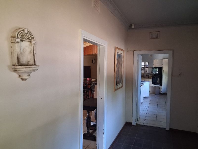 A view through a hallway connecting to a kitchen and living area, featuring tiled flooring and decorative wall molding.
