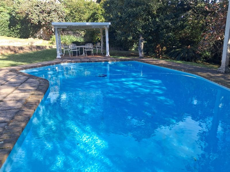 A private swimming pool area featuring a paved surround and a shaded pergola structure set within a landscaped garden.