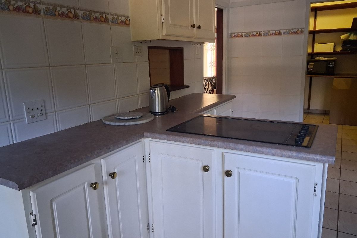 A functional kitchen featuring white cabinetry, laminate countertops, and an integrated electric hob with tiled splashbacks and flooring.
