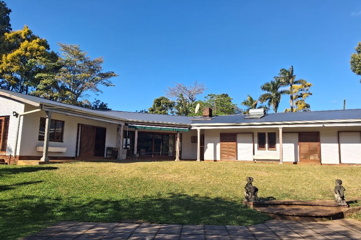 Spacious rear exterior view of the house featuring a large lawn, paved patio area, and classic brick facade with wooden shutters.