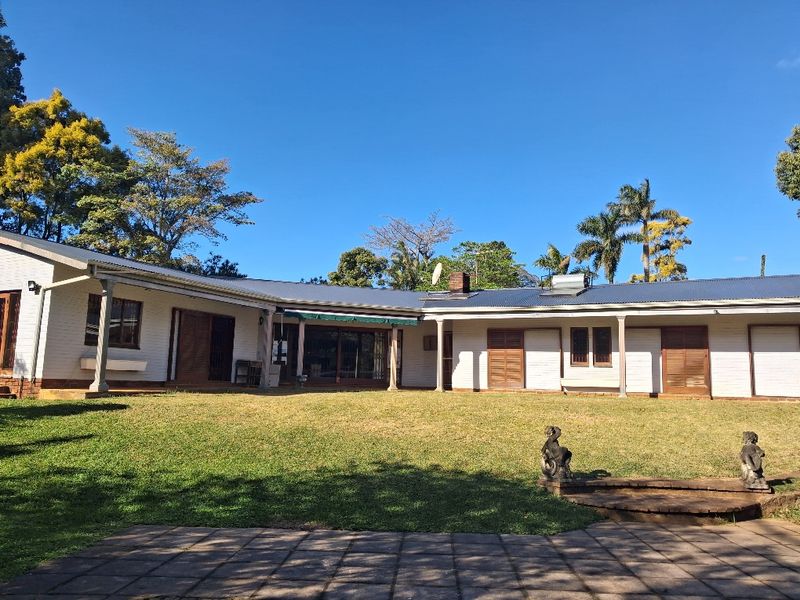Spacious rear exterior view of the house featuring a large lawn, paved patio area, and classic brick facade with wooden shutters.