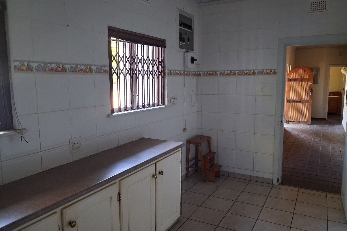 A functional kitchen space featuring tiled walls and flooring, built-in cabinetry, and a window with security bars, offering potential for modern renovation.