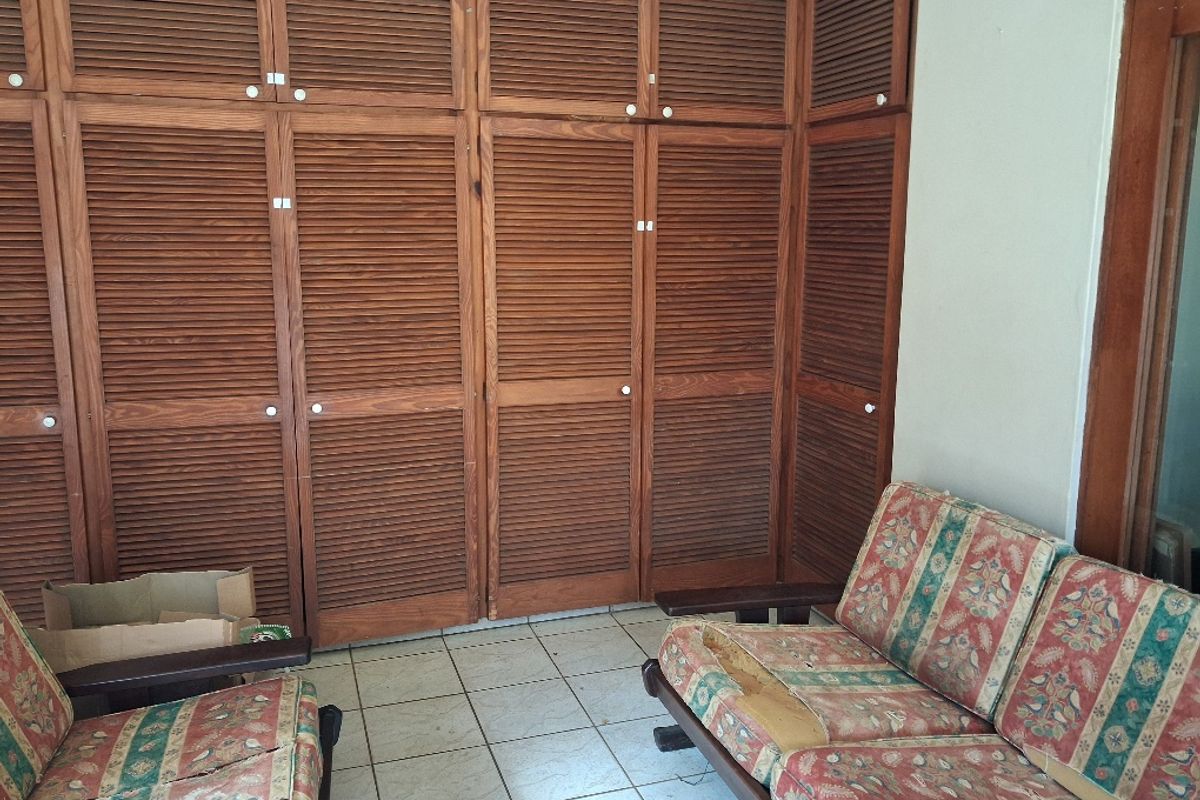 Bedroom featuring extensive built-in wooden louvered cupboards and tiled flooring, offering significant storage space in need of cosmetic updates.