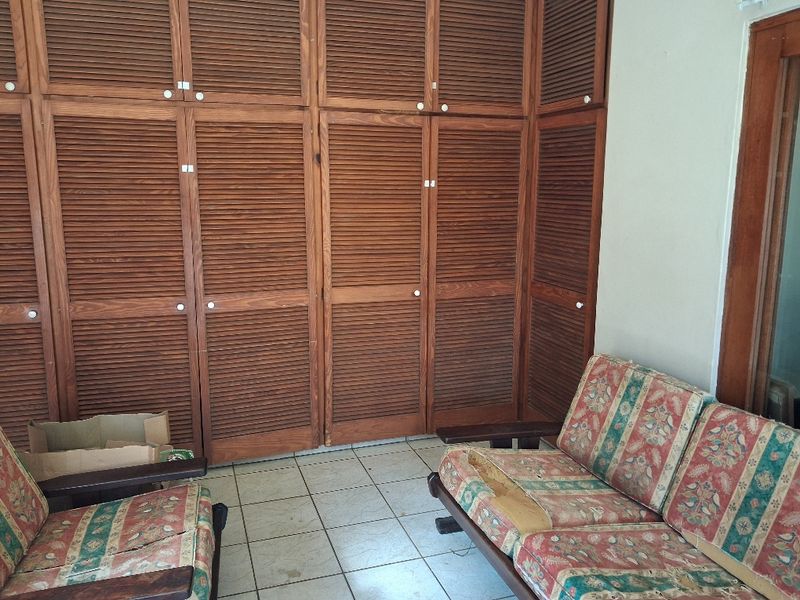 Bedroom featuring extensive built-in wooden louvered cupboards and tiled flooring, offering significant storage space in need of cosmetic updates.
