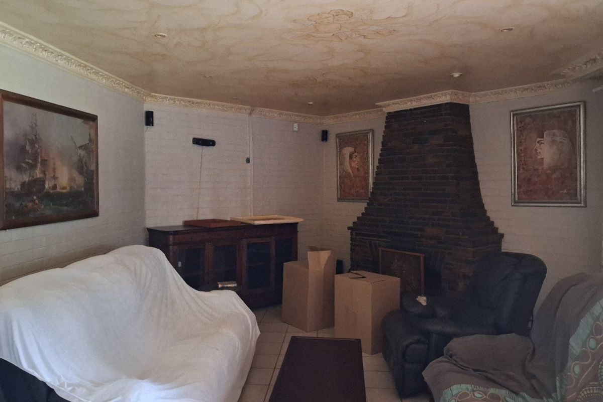 A living room featuring a prominent brick fireplace, decorative ceiling molding, and tiled flooring, offering a traditional layout with potential for modernization.