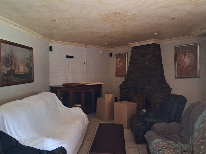 A living room featuring a prominent brick fireplace, decorative ceiling molding, and tiled flooring, offering a traditional layout with potential for modernization.
