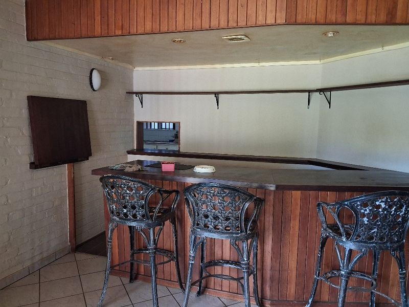 A dedicated bar area featuring a built-in timber counter, tiled flooring, and wall-mounted shelving, offering potential for a modern entertainment space update.
