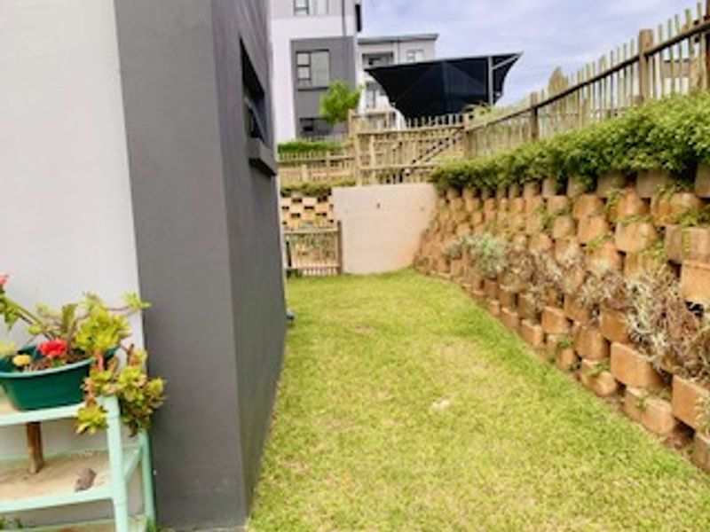 A side garden area featuring a tiered retaining wall, timber fencing, and a grass lawn adjacent to the apartment building exterior.
