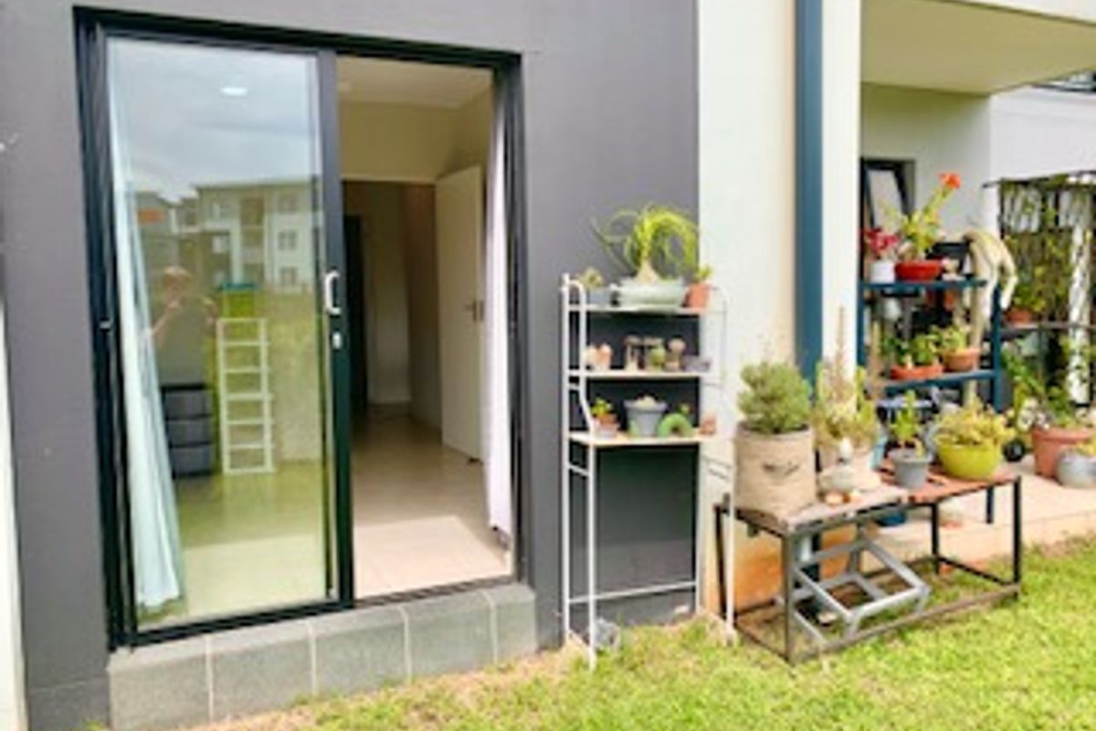 Ground floor apartment exterior featuring a sliding glass door entrance leading to a small patio area and garden space.