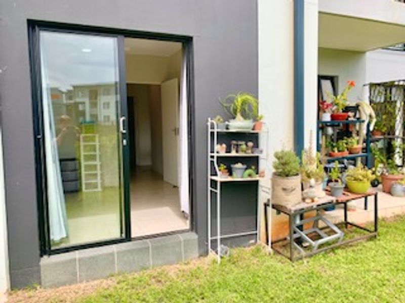 Ground floor apartment exterior featuring a sliding glass door entrance leading to a small patio area and garden space.