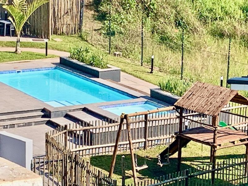 Outdoor pool area featuring a swimming pool with tiled surround, raised garden beds, and a wooden play structure set within a fenced garden.