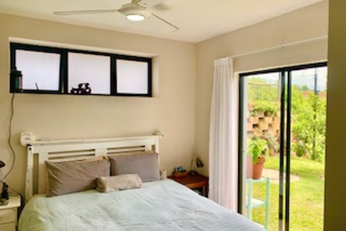A bedroom featuring a ceiling fan, horizontal window, and sliding glass door providing direct access to the garden area.
