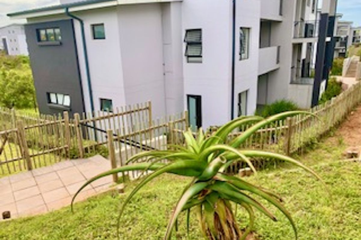 Rear view of a modern apartment building featuring a paved patio area and metal perimeter fencing.