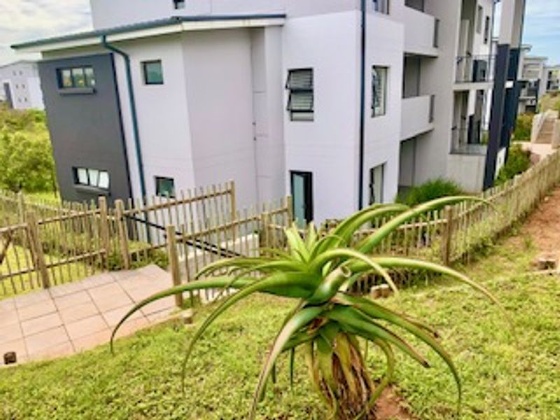 Rear view of a modern apartment building featuring a paved patio area and metal perimeter fencing.