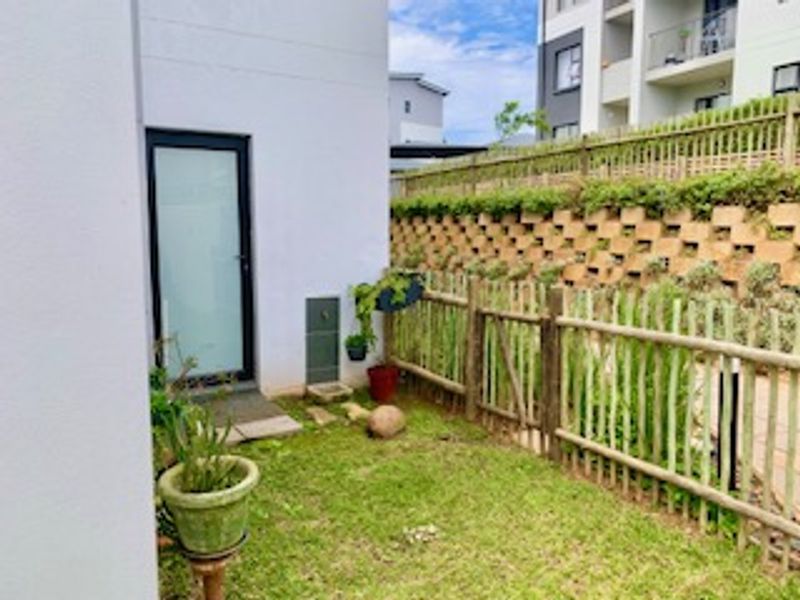 A private rear garden area featuring a retaining wall, timber fencing, and direct access to the apartment via a glass panel door.