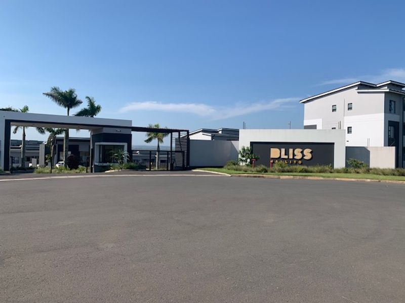The entrance to the Bliss Ballito complex, featuring a modern security gatehouse, paved driveway, and clear estate signage.