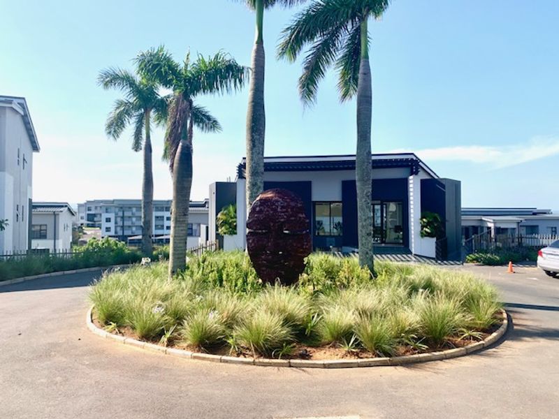 A well-maintained entrance roundabout featuring mature palm trees and modern architectural facade elements, providing a welcoming approach to the apartment complex.
