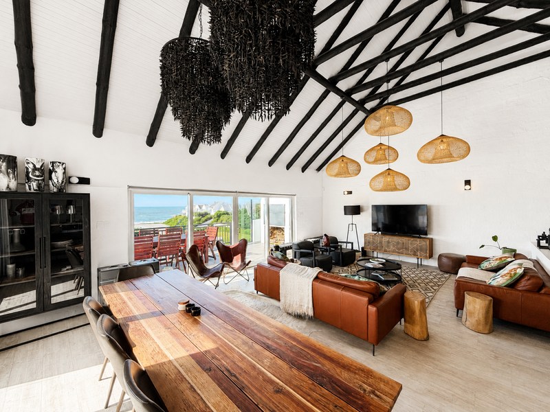 Spacious open-plan living and dining area featuring a vaulted ceiling with exposed timber rafters, tiled floors, and large sliding doors opening to a balcony.