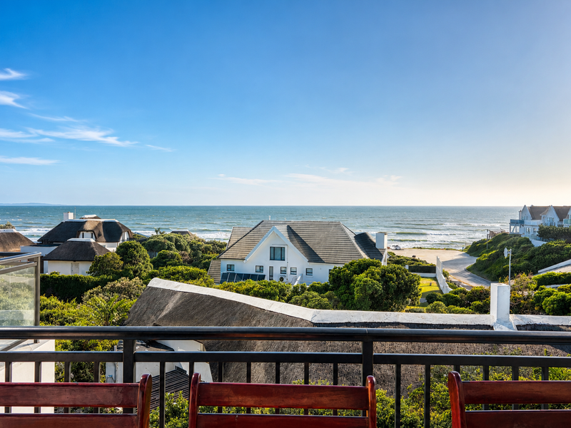 A scenic elevated view overlooking coastal homes, lush greenery, and the ocean horizon from a balcony.