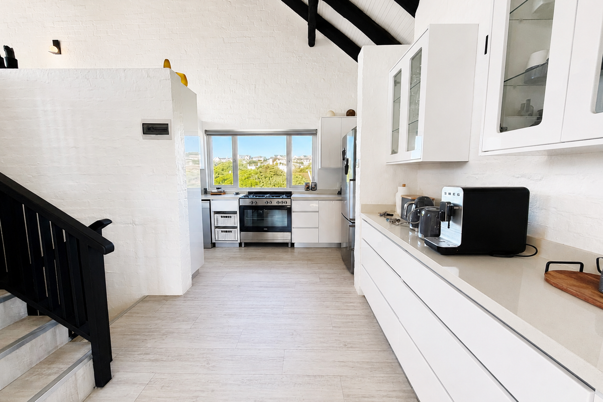 Modern kitchen featuring white cabinetry, stone countertops, gas stove, and vaulted ceilings with exposed timber beams, creating a bright and airy culinary space.