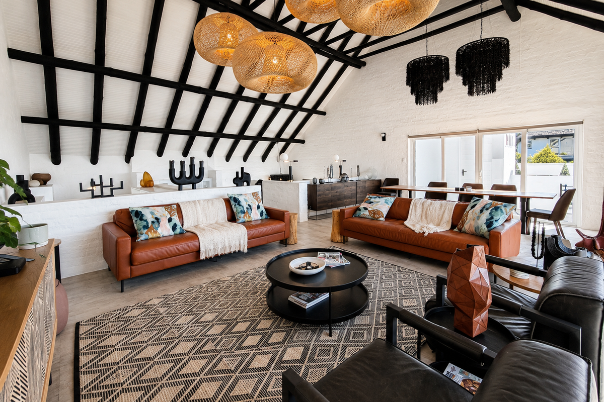Spacious living area featuring a high vaulted ceiling with exposed timber rafters, painted brick walls, and large sliding glass doors leading to the exterior.