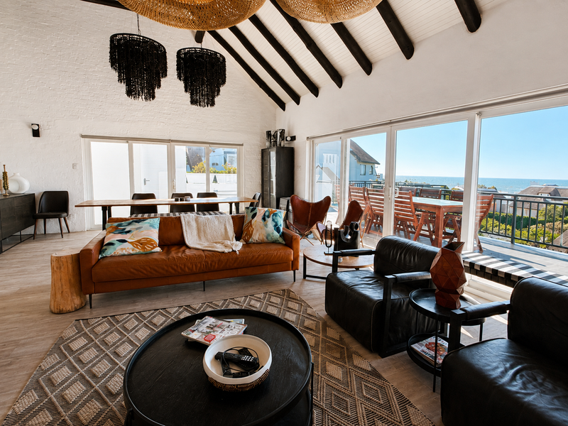 Spacious open-plan living area featuring a vaulted ceiling with exposed timber beams, large sliding glass doors, and views of the ocean.