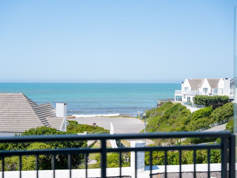 A scenic elevated view overlooking the coastline, ocean, and surrounding residential properties, captured from a balcony with a modern glass and metal balustrade.
