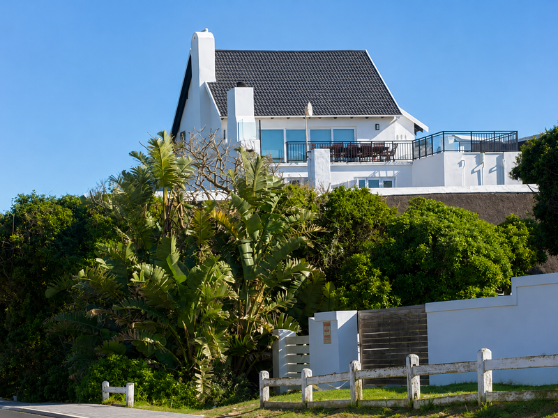 A well-maintained multi-level house featuring a tiled roof, chimney, and a spacious balcony with metal railings, set behind a secure boundary wall.